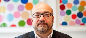 Headshot of Professor de Paula, white man, bald, with beard, with glasses on, against a colourful background